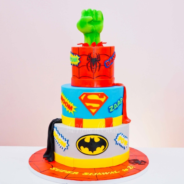 a multi layered superheroes cake with a green Hulk hand on top