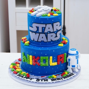a blue cake with a toy robot on it star wars and lego theme